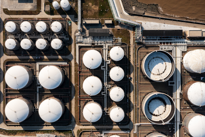 Drone Aerial view Oil ship tanker load or unload oil at loading dock from Large Tank warehouse with Terminal commercial port and cityscape background for transportation on the sea.